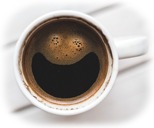 Tasse Kaffee auf weißen Tisch von oben in weißer Tasse. Die Crema im Kaffee hat eine Form wie ein Smiley Gesicht beziehungsweise zwei Augen und ein lächelnder Mund.
