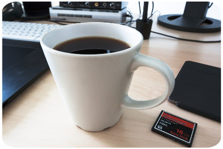 Weisse Tasse mit Kaffee auf dem Schreibtisch und daneben sind Bildschirmtastatur, Telefon und externer Speicherchip zu sehen.