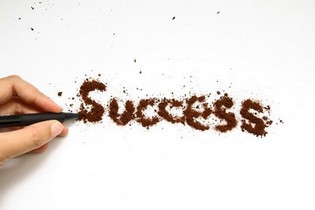 Hand mit Stift zeigt auf das Wort Success aus gemahlenem Kaffee